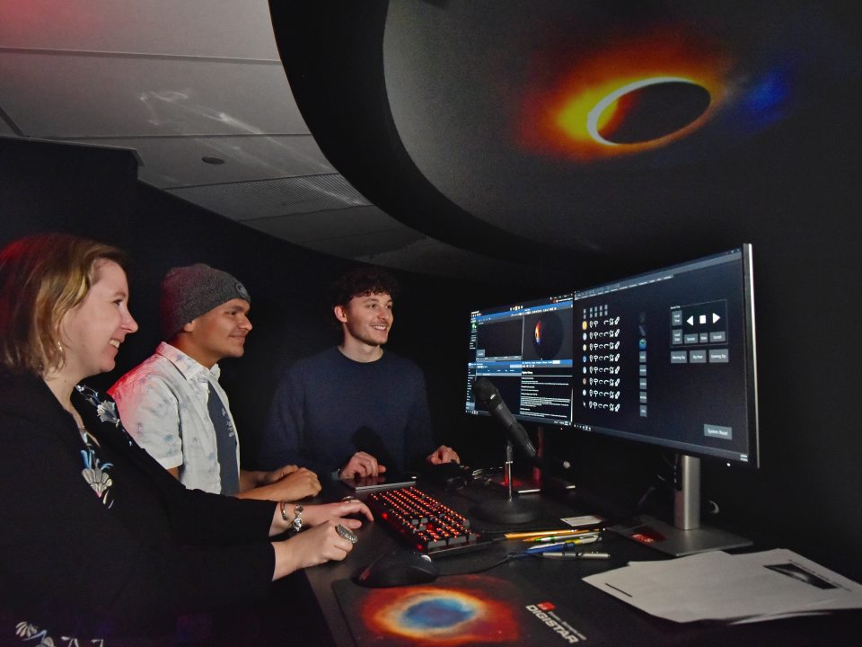 Students and a faculty member operate computers and visualization software inside the campus planetarium.