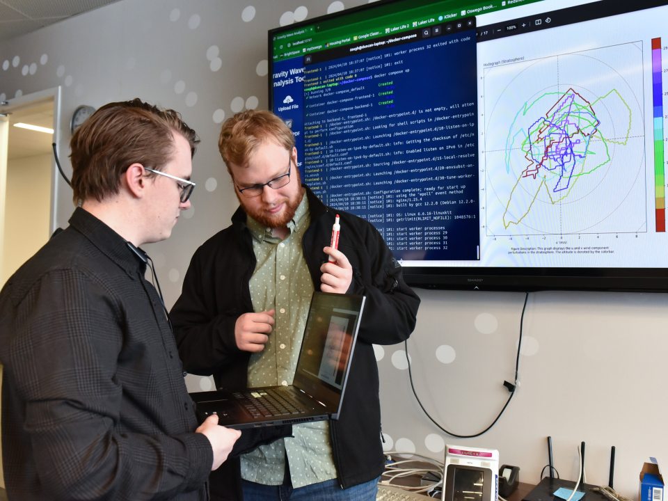 Two students review code and data visualizations on a screen while working together on a computer science project.