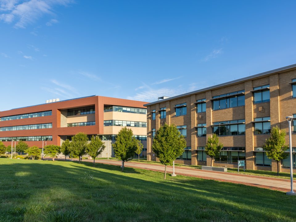The Richard S. Shineman Center stands on SUNY Oswego’s campus, featuring modern architecture, solar panels, and a prominent vertical sign in a landscaped green space.
