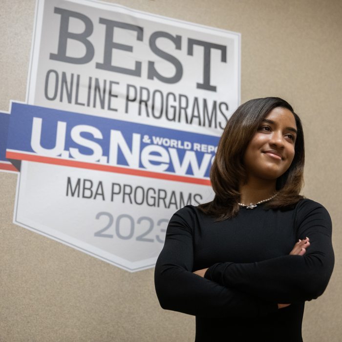 A woman standing in front of a sign, "U.S. News & World Report, Best online MBA programs 2023"