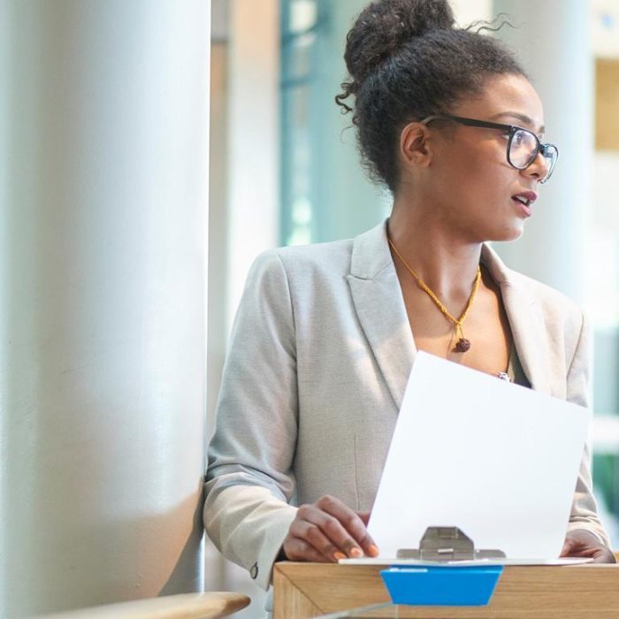 A woman in a gray suit jacket, holding a clipboard
