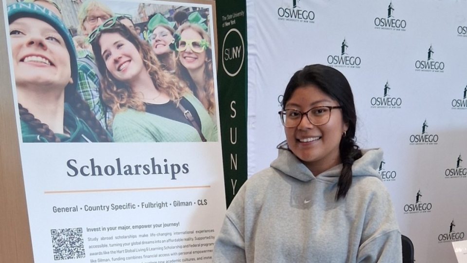 A female student standing in front of a poster about scholarships 