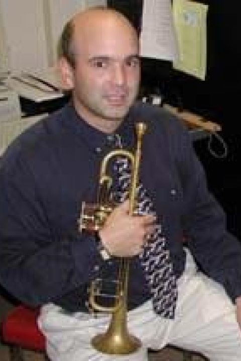 Terry Caviness holding a wind instrument with black shirt and white pants on