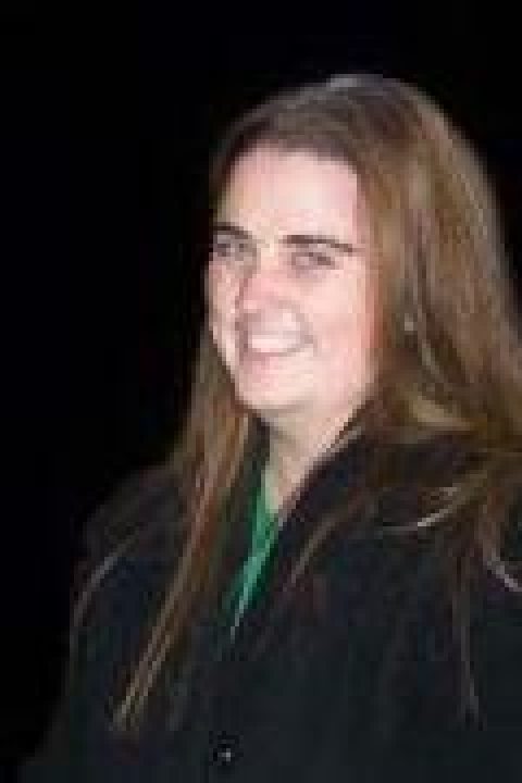 Colleen Dailey is smiling, with a green shirt on with a black jacket on top