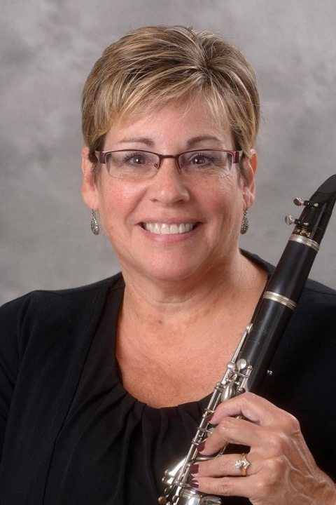 An image of Deb Farden, who wears glasses and has short blonde hair holding a wind instrument.