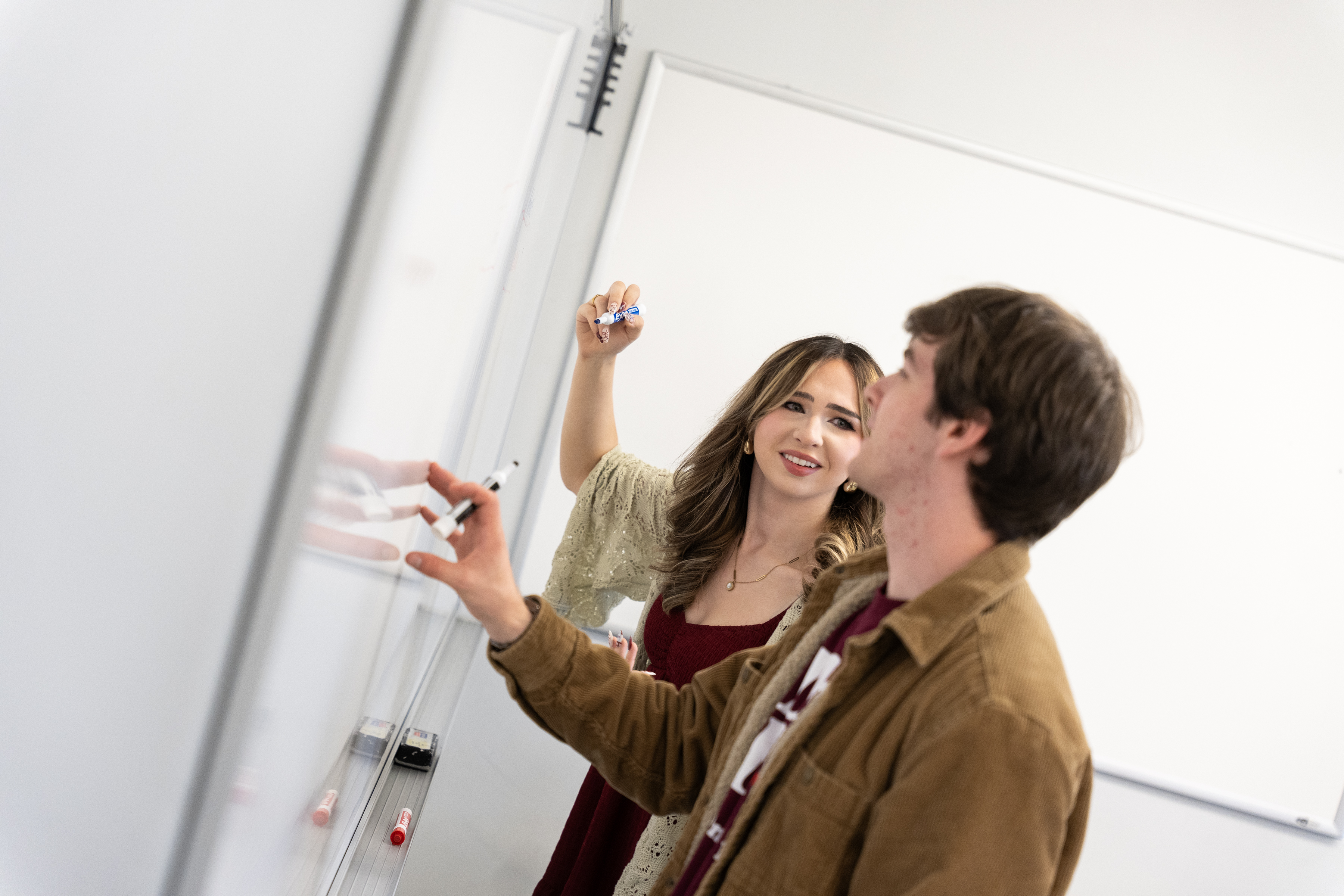 Two SUNY Oswego students collaborate at a whiteboard, writing and discussing ideas during a class activity.