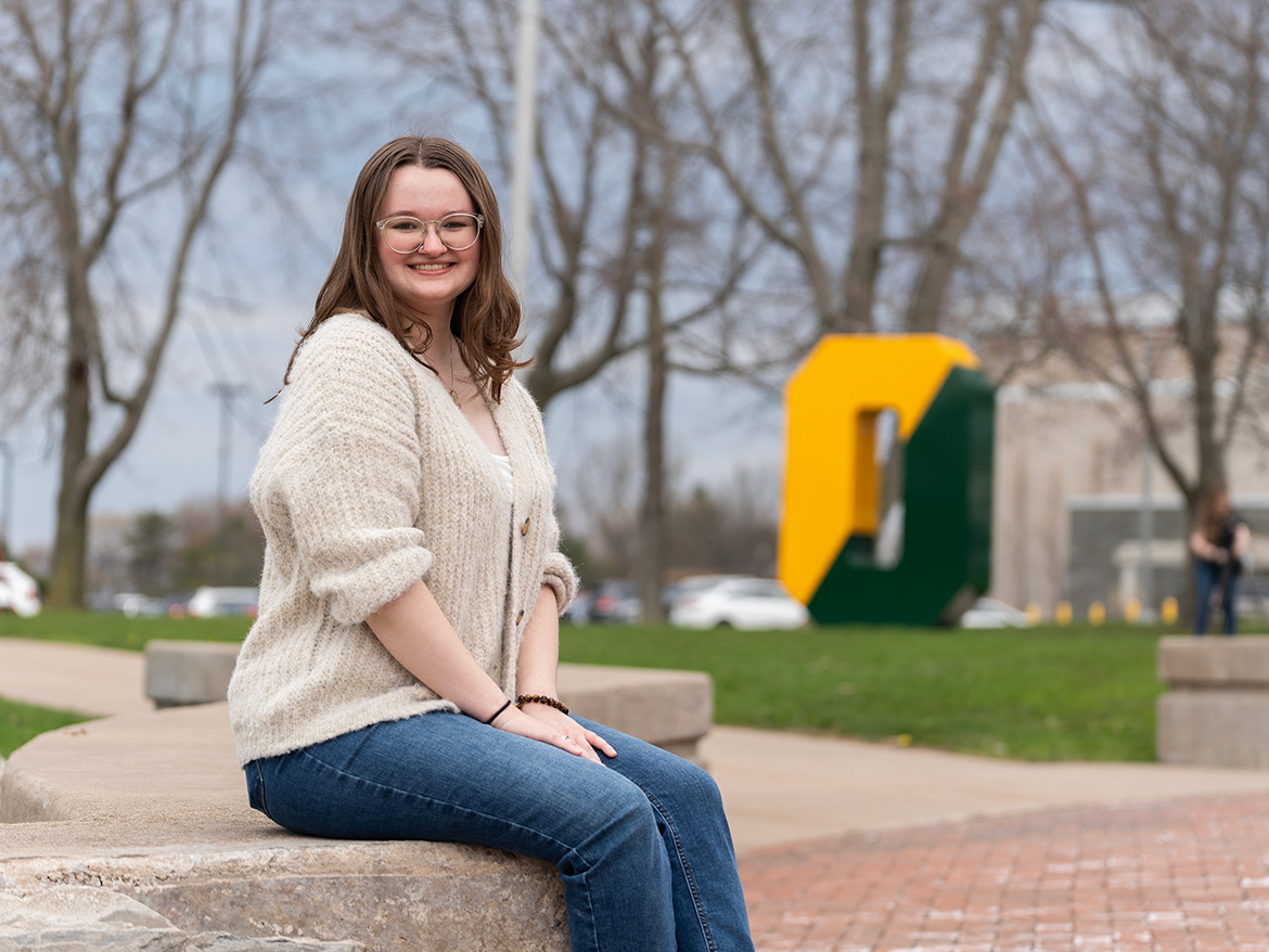 student posing by the spirit o on the quad