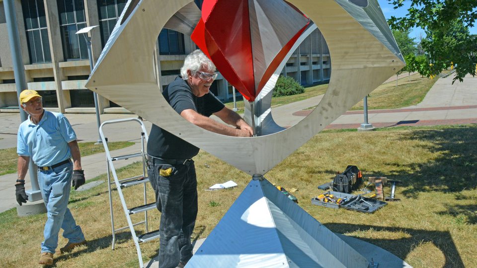 Artist Bob Turan with his sculpture that features a pinwheel in a box upon a pyramid