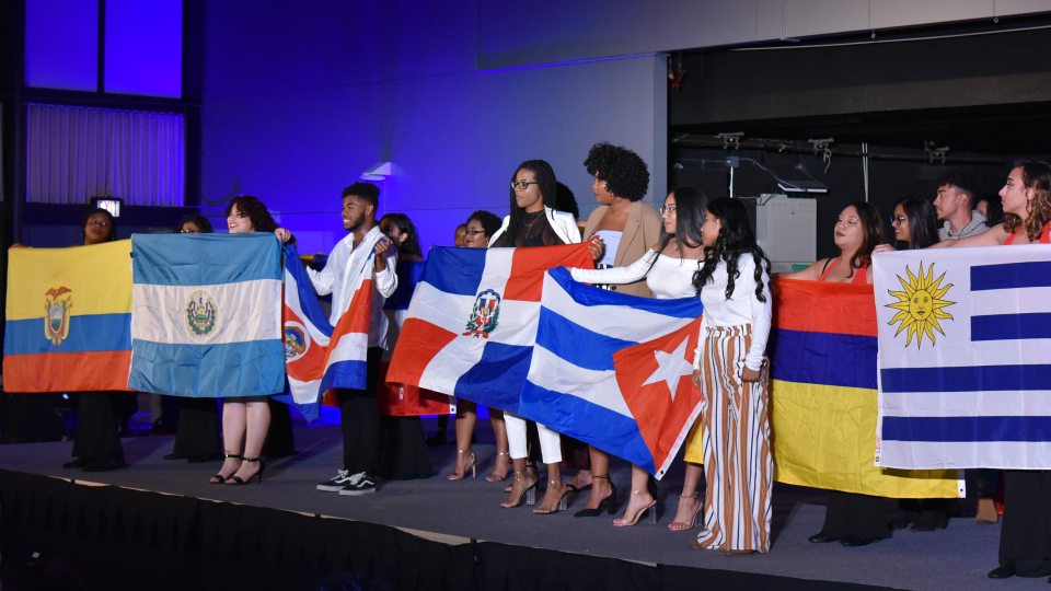 Students hold flags of many nations at 2018 ALANA Fashion Show