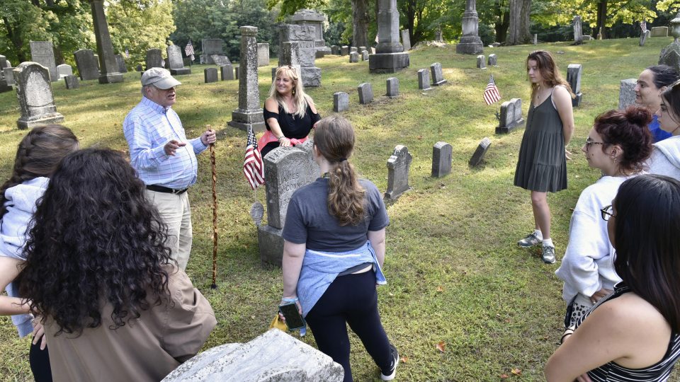 Oswego Town Historian (and 1966 SUNY Oswego alumnus) George DeMass speaks with theatre faculty member Jonel Langenfeld (center) and students from the college's storytelling class as they prepare for a family-friendly cemetery storytelling tour Oct. 29
