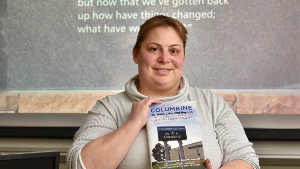 Jackie Schildkraut with book on 20th anniversary of Columbine, with quote from healing wall on screen behind her