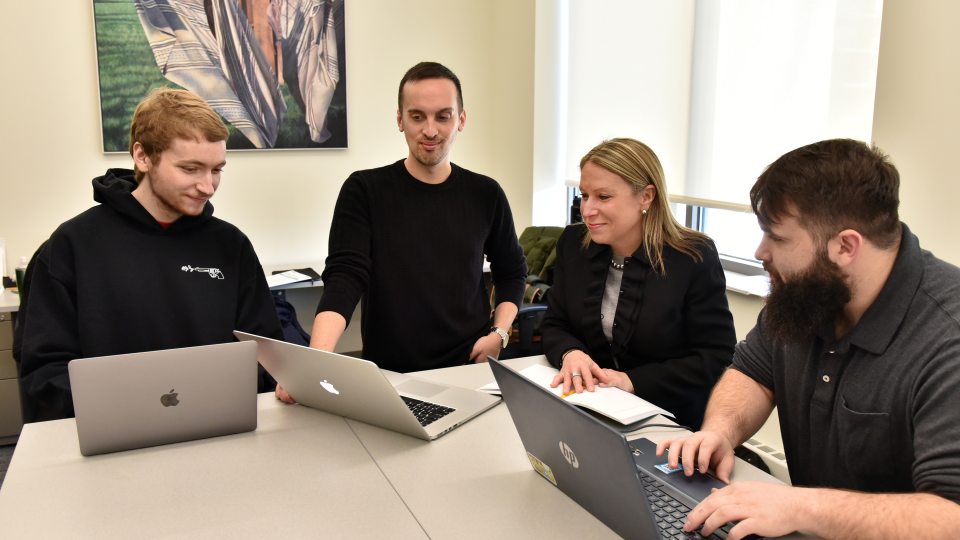 Three school psychology master's students and a faculty member look over some work on laptops