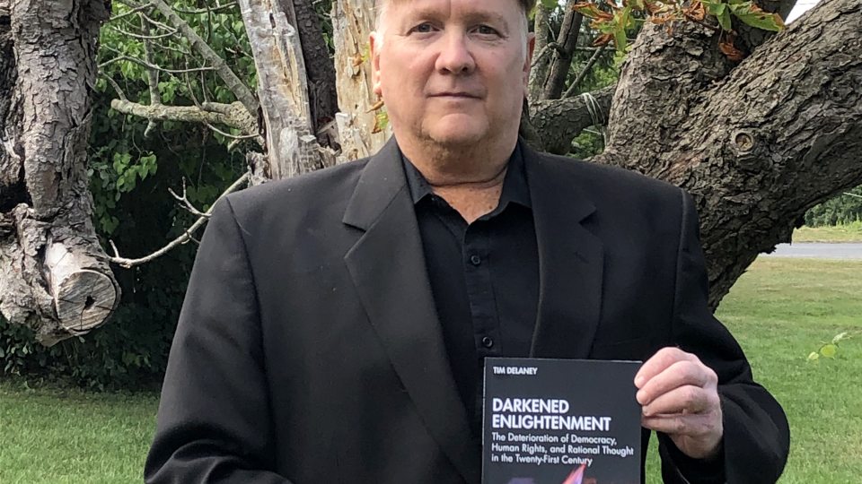 Tim Delaney holding new book, Darkened Enlightenment