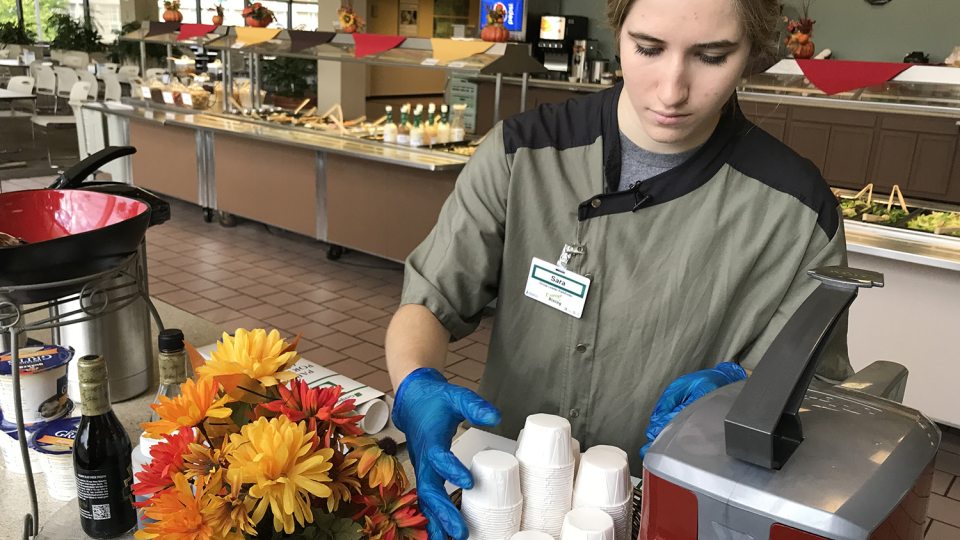Sara Meal refills paper condiment cups in a dining hall