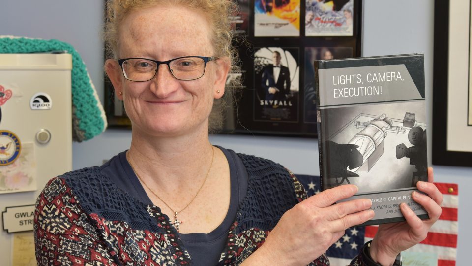 Helen Knowles with book Lights, Camera, Execution, a collaboration of three faculty members