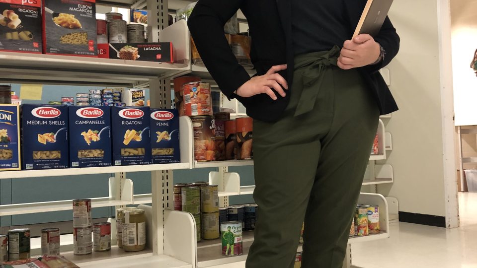 Senior Helena Buttons, SHOP Coordinator, standing in front of shelves with food at SHOP