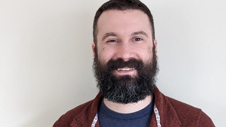 Headshot of Remmington Johnson wearing a maroon button up. Remmington has dark brown hair that is salt and pepper with a beard