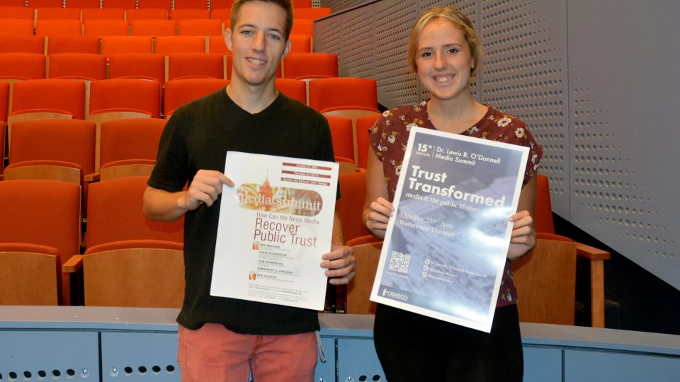 Josh Holfoth and Tori Kammer holding posters from the first media summit in 2005 and the 2019 edition