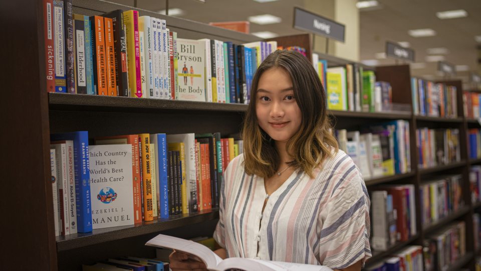 SUNY Oswego student Naw Ka Paw Paw, who earned a position in SUNY’s 2022 Premedical Opportunity Program, is shown among stacks of medical books
