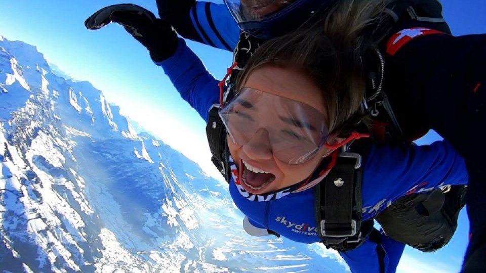 Student skydiving above the Alps, wearing look of exhilaration