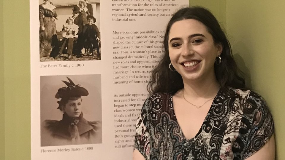 SUNY Oswego recent graduate Gabrielle Belmont stands next to her curated exhibit at the Richardson-Bates House Museum