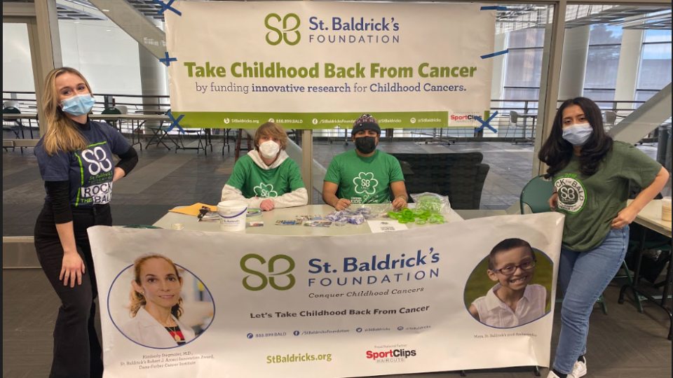 Group of four students work a table with St. Baldrick's banners to support the children's cancer charity