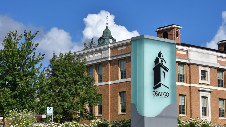 SUNY Oswego sign with background of Sheldon Hall