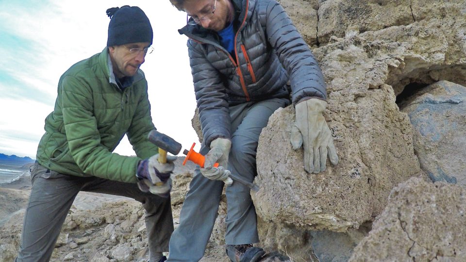 Faculty member Justin Stroup helps collect rock samples on a mountain