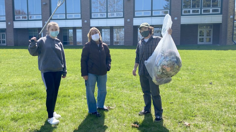 Three students show off some of what they've cleaned up as part of a campus effort