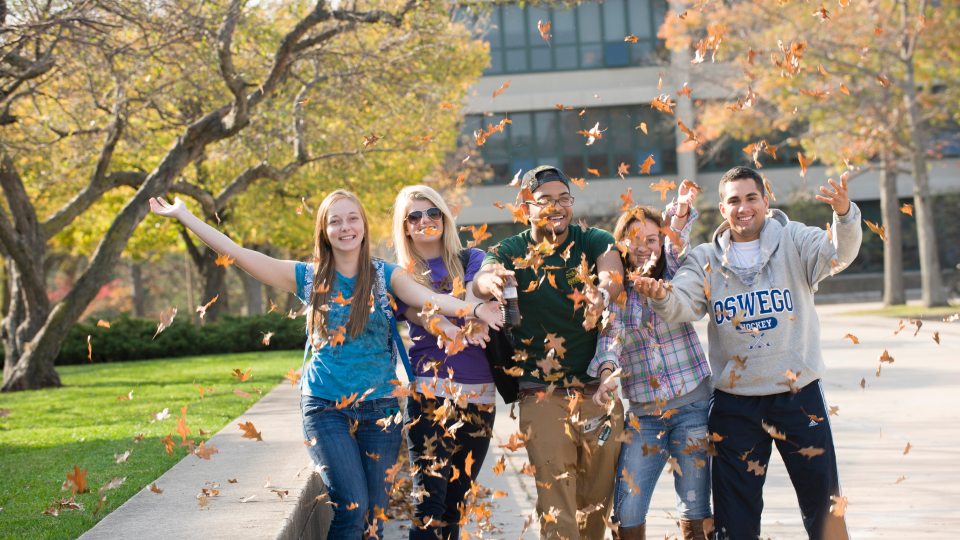 SUNY Oswego students toss leaves in the air to celebrate the fall season.