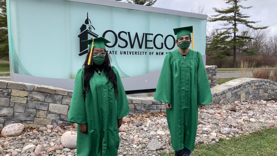 Taylor Clark and Daniel Garcia next to SUNY Oswego entrance sign