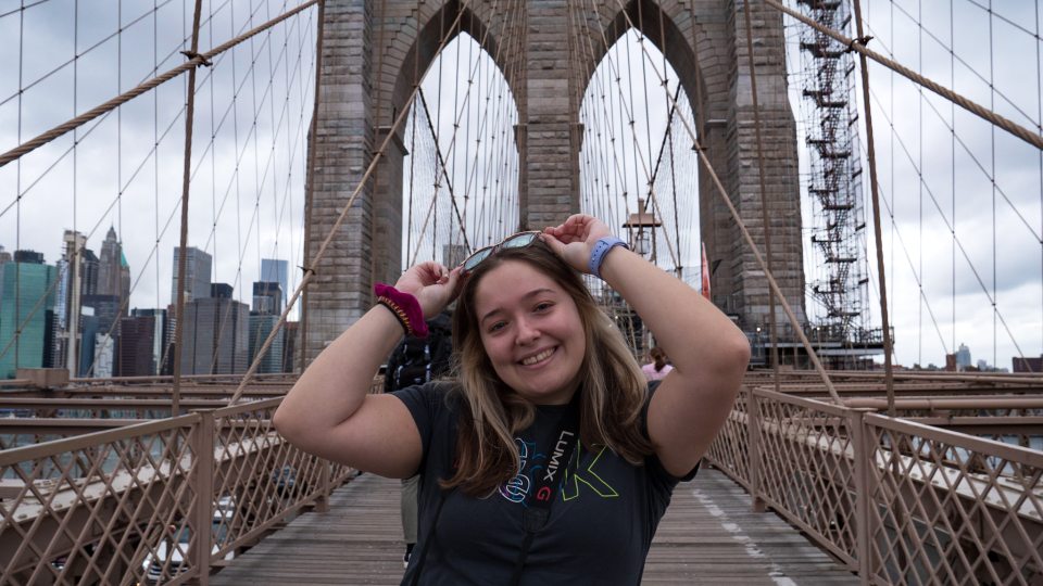 Alum Corey Cesare smiling with a camera on the Brooklyn Bridge.