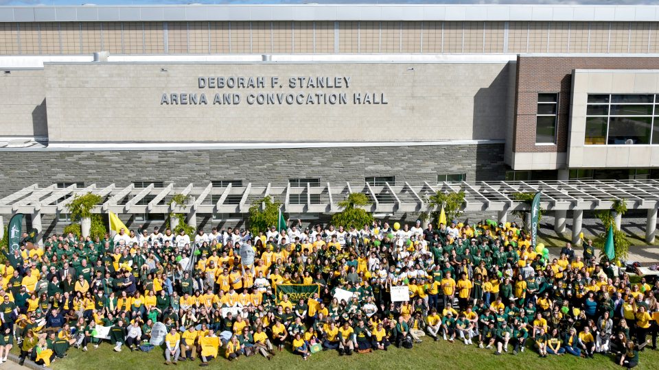 Many members of the Oswego family pose in front of the new sign for the Deborah F. Stanley arena and convocation hall for the 2021 Green and Gold Day photo