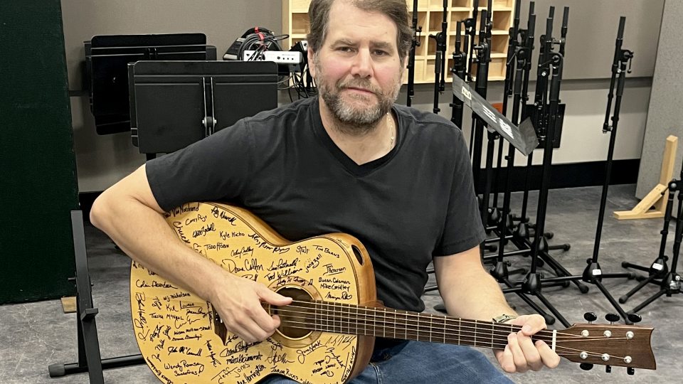 Tim Herron with the signature-covered guitar of the Oswego Guitar Project in a Tyler Hall studio