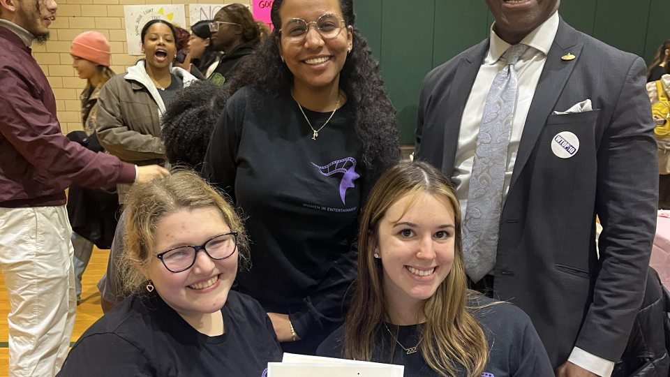 Student executive board members of the Women In Entertainment Club pose for a photo with President Nwosu at their Student Involvement Fair table.