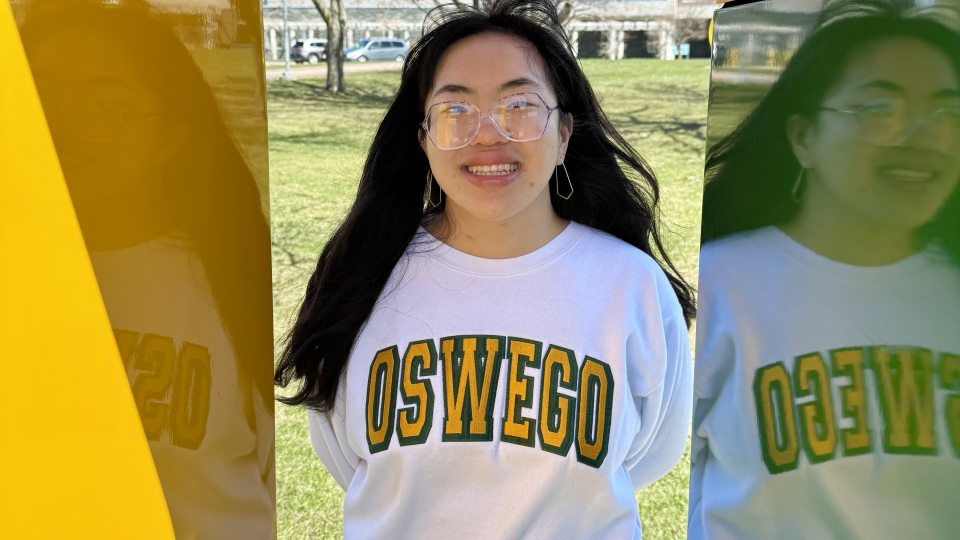SUNY Oswego student Emma Halsey stands inside the green and gold "O" statue on SUNY Oswego's campus.