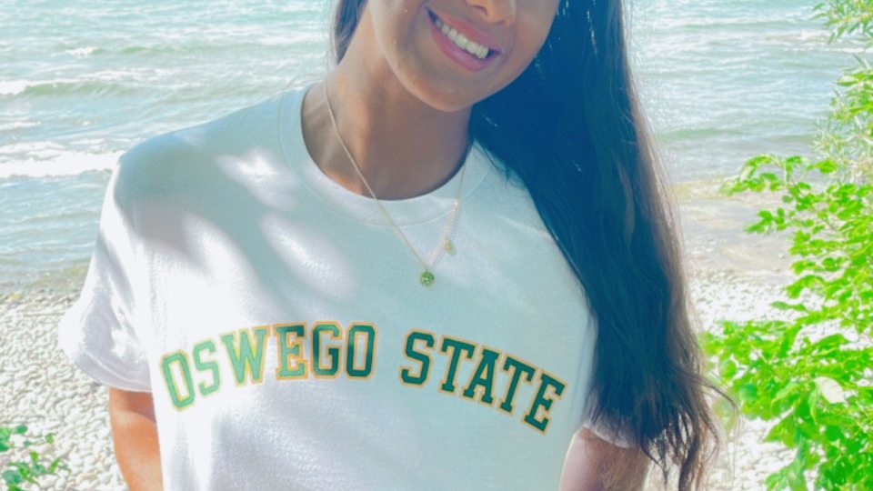 Jolie Santiago poses by Lake Ontario in a white Oswego State T-shirt