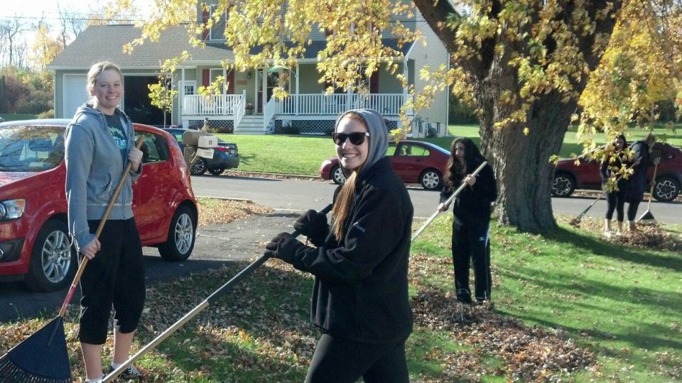 Student-athletes collecting leaves in a front yard