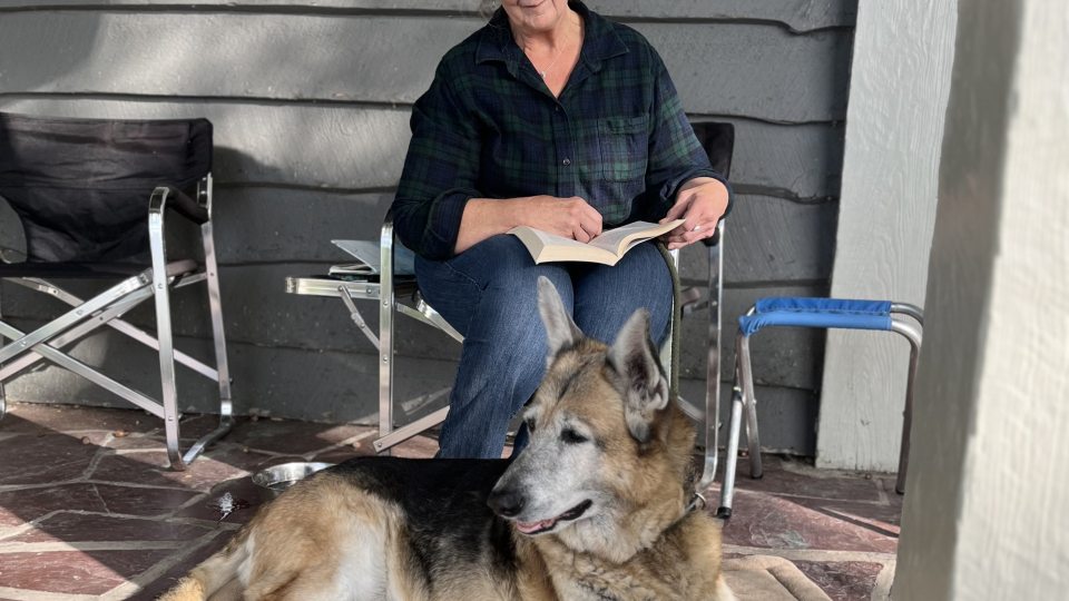Linda Knowles reads on a porch with dog