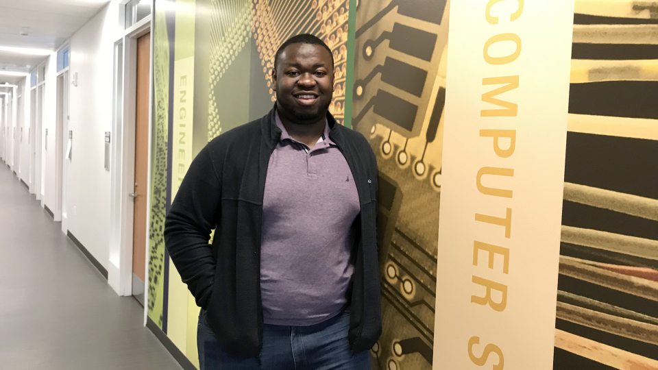Kingsley Ibezim in front of a mural on computer science and other fields in the Shineman Center