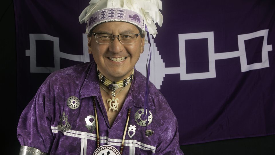 Storytellers Perry Ground stands in front of the Haudenosaunee flag