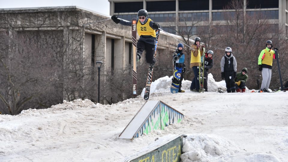 Skiers and snowboarders smile while standing atop a giant snow mound at a past Rail Jam
