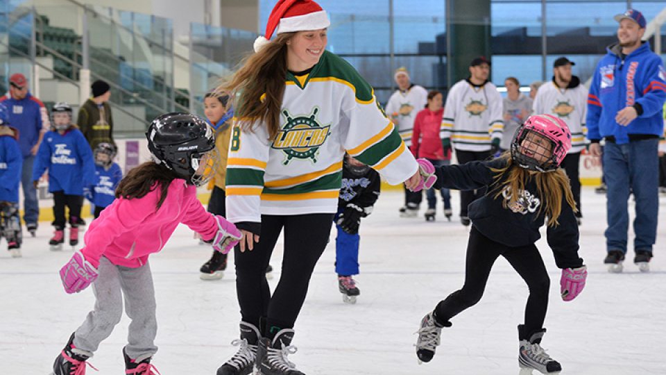 Two little girls skate with a women's hockey player