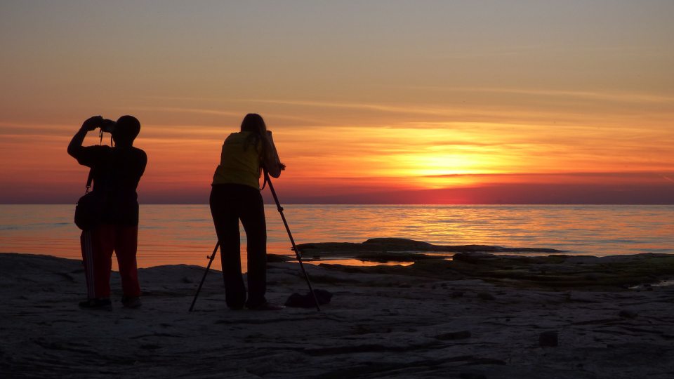 Two people take photographs on the shore of Lake Ontario