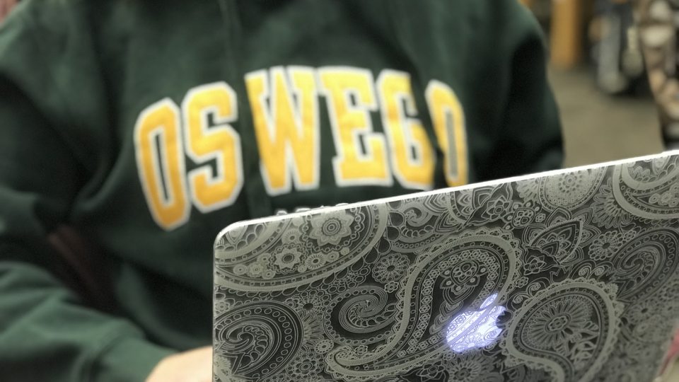 Student with an Oswego hoodie using a laptop computer