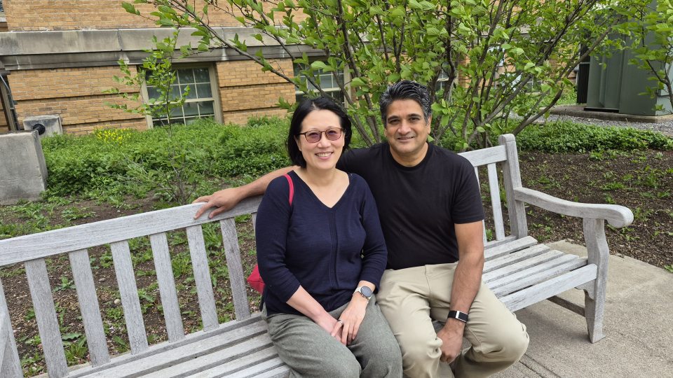 Julie Oh and Neelesh "Neel" Shah sit on a bench in front of Sheldon Hall