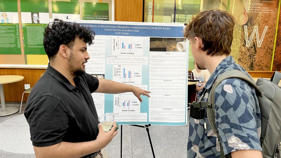 Dominic Bachtler explains the research poster, “Measuring Boldness in Round Gobi (Neogobius melanostomus) Using Exit Assays,”at the Fall 2026 Scholarly and Creative Activities Poster Symposium