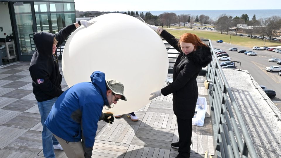 Kaitlin Farrell (at right) helps prepare a weather balloon during a research session on the roof of SUNY Oswego's Shineman Center.