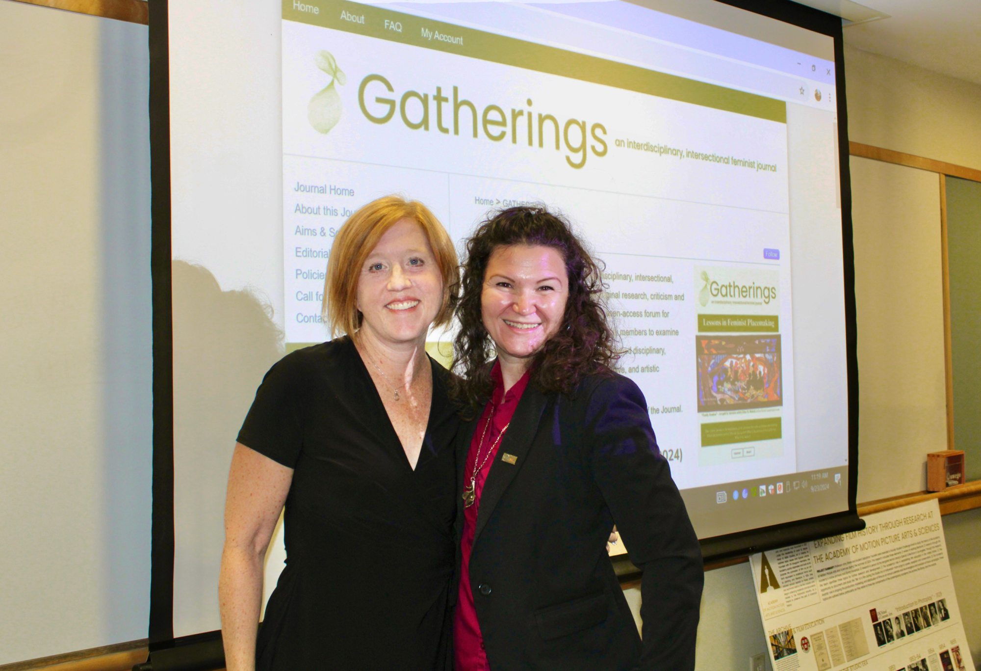 Cinema and Screen Studies professor Dr. Amy shore and English and Latin American studies studies professor Dr. Roberta Hurtado stand in front of the website for "Gatherings: An interdisciplinary and intersectional feminist journal."