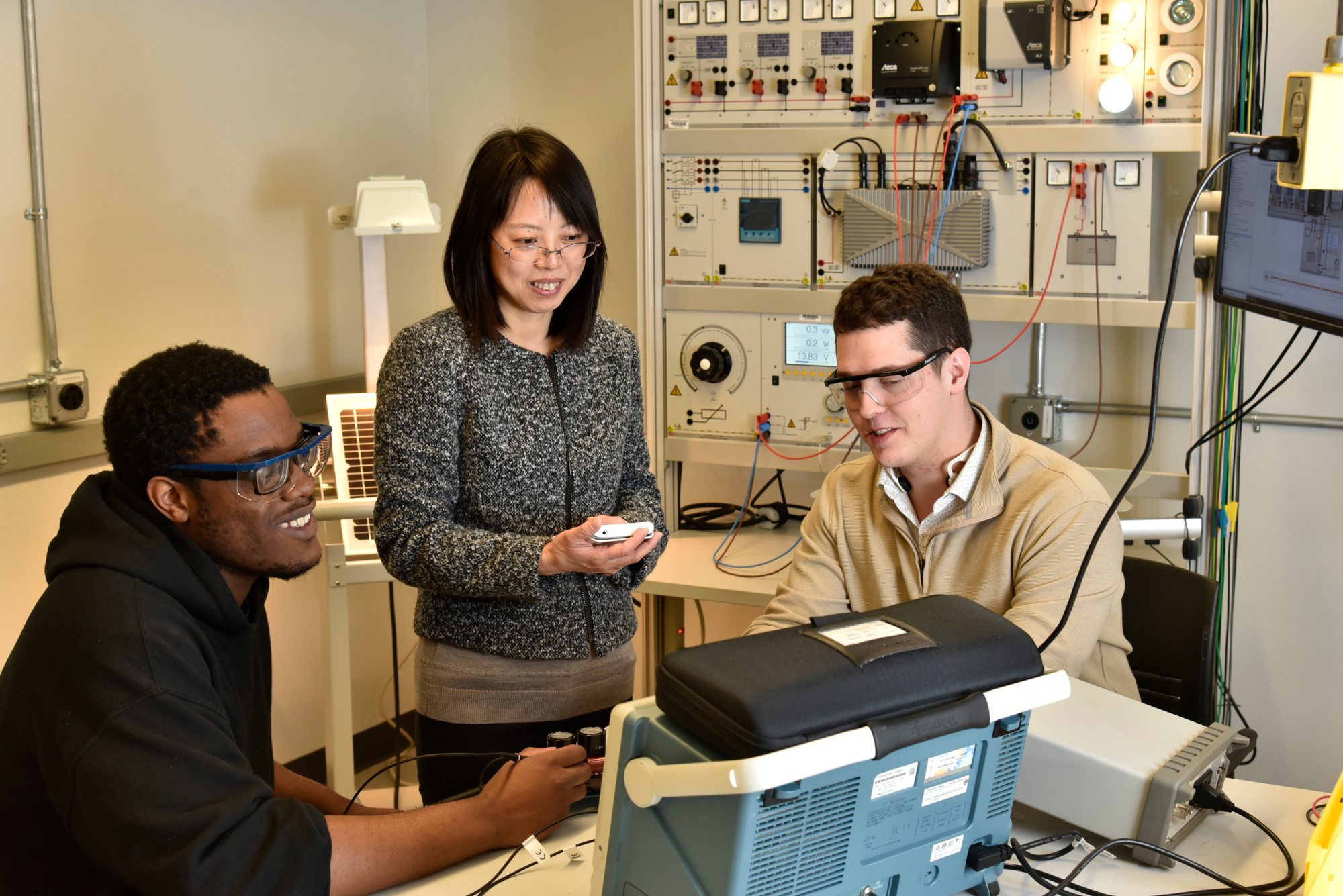 ECE faculty member Hui Zhang (standing), works with students (from left) Chibuike Ogbonna and Avery Croucher in spring 2022, after earning National Science Foundation funding for research related to improving the charging of electric vehicles.